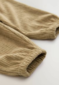 Ribbat beige tyg med elastiska manschetter, med en texturerad yta. Designen betonar en avslappnad passform och mjukt material.
