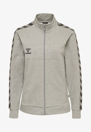 Veste de sport zippée grise avec un col montant, en tissu texturé et accents en chevron noir le long des manches. Logo sur la poitrine gauche.