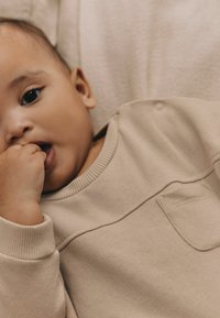Beige színű baba pulóver kerek nyakkivágással, bordás mandzsettákkal és egy kis elülső zsebbel. Puha tapintású, egyszerű, minimalista dizájn.