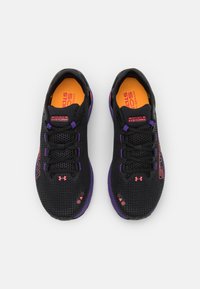 Baskets de course Under Armour Sonic 6 Storm noires avec des accents violets et des semelles oranges, vues de dessus sur un fond blanc.