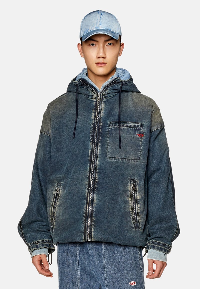 Jeansjacke mit Kapuze in verblasstem Blau, mit einem Frontreißverschluss, elastischen Bündchen und Seitentaschen. Getragen über einem hellblauen Hemd und kombiniert mit Jeans.