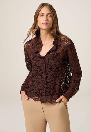 Blusa in pizzo marrone con motivo floreale, apertura con bottoni e design con colletto. Maniche lunghe con dettaglio a scallop sul bordo. Tessuto testurizzato.