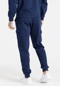 Mörkblå cargo-joggers tillverkade av mjukt tyg, med sidofickor, elastisk midja och mudd vid anklarna. I kombination med vita sneakers.