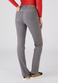 Pantalones de mezclilla gris con un diseño de pierna recta, que presentan dos bolsillos traseros y un parche de cuero en la cintura. Combinados con zapatillas de deporte con patrones.