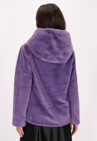Lilla faux fur jakke med hætte, der har en blød tekstur og lange ærmer. Designet er enkelt og afrundet i kanten.