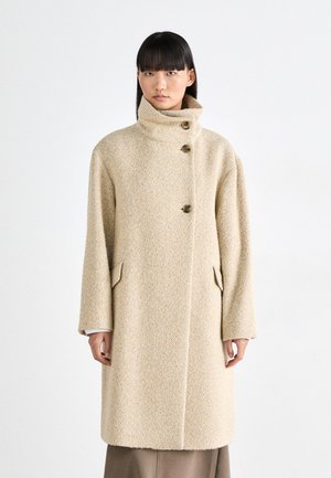 Beige wollen jas met een hoge kraag, drie knopen en twee zijzakken. Tweedtextuur met een visgraatmotief.