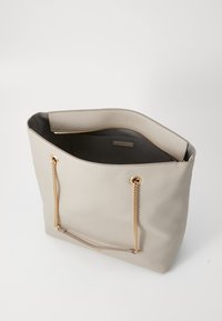 Beige faux leather tote bag with gold chain straps. Open top, lined interior, features a zippered pocket inside. Smooth texture, rectangular shape.