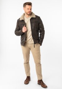 Bruine leren jas met een schapenvachtkraag, ritssluiting en zijzakken. Draag het over een licht sweater en combineer het met tan kleurige broeken en bruine laarzen.