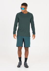 Idrottskläder med en långärmad mörkgrön skjorta och turkosa shorts. Inkluderar blå solglasögon och svarta cykelskor. Lättviktsmaterial.