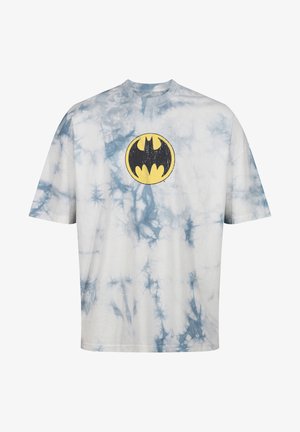 T-shirt bianco con motivo tie-dye blu. Presenta un logo giallo di Batman centrato sul petto. Collo rotondo, maniche corte, vestibilità rilassata.