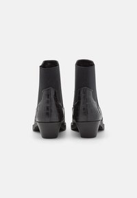 Botas negras hasta el tobillo con una suave textura de croc-embossed, paneles laterales elásticos y un pequeño tacón apilado. La vista trasera muestra los detalles y la costura.