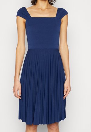 Marineblauwe geplooide jurk met korte mouwen, een vierkante halslijn en een getailleerd lijfje, gemaakt van een gladde, lichte stof.