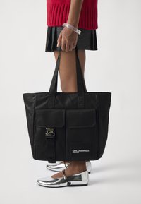 Svart läder toteväska med två framfickor, silverfärgad hårdvara och präglade handtag. Åtföljs av metalliska silverfärgad flats.