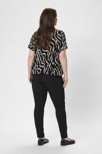 Černý a béžový pruhovaný krátký rukáv top spojený s černými skinny kalhotami a plochými černými botami, pohled zezadu.