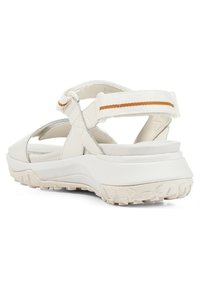 Vita sportiga sandaler med en texturerad gummisul och justerbara remmar, samt en orange accent. Öppen design med ett stödjande hälskydd.