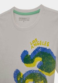 Svjetlosiva majica od organskog pamuka. Sadrži apstraktne plave i zelene uzorke s natpisom "LOS ANGELES" u svijetloj žutoj boji. Okrugli izrez s zelenim rubom.