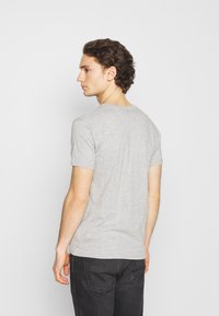 Camiseta gris de manga corta hecha de algodón, con un clásico cuello redondo y una textura suave, combinada con jeans oscuros.