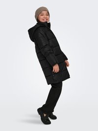 Black puffer jacket with texture detailing, hood, and front buttons, paired with black pants and glossy shoes, set against a light background.