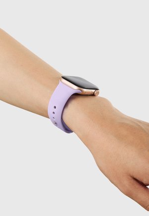 Smartwatch mit schwarzem Bildschirm und roségoldenem Rahmen, getragen am Handgelenk mit einem lavendelfarbenen Silikonarmband vor einem einfarbigen grauen Hintergrund.