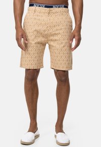 Pantalones cortos para hombre en un color beige claro con un patrón geométrico blanco. Fabricados con un tejido suave, cuentan con un cierre de botón y un logo en la cinturilla.