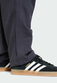 Sorte ruskind Adidas Gazelle sneakers med tre hvide striber, kombineret med mørkegrå bukser med sidesømme og en afslappet pasform.