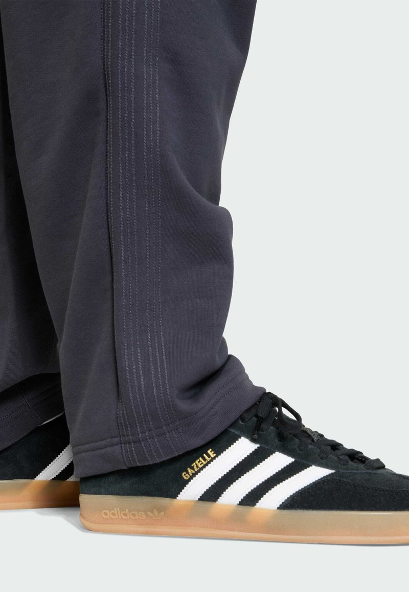 Sorte ruskind Adidas Gazelle sneakers med tre hvide striber, kombineret med mørkegrå bukser med sidesømme og en afslappet pasform.