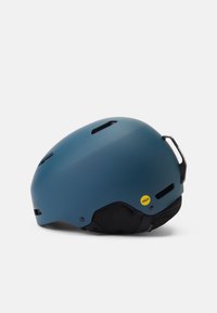 Blauwe matte helm met zwarte binnenpadding, ventilatieopeningen en een MIPS-sticker aan de zijkant. Gestroomlijnd ontwerp en verstelbare gespsluiting.