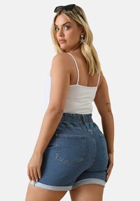 Jeansshorts med en ljusblå tvätt, elastisk midja, uppvikt nederkant och två bakfickor. Matchas med en vit ärmlös topp och solglasögon.