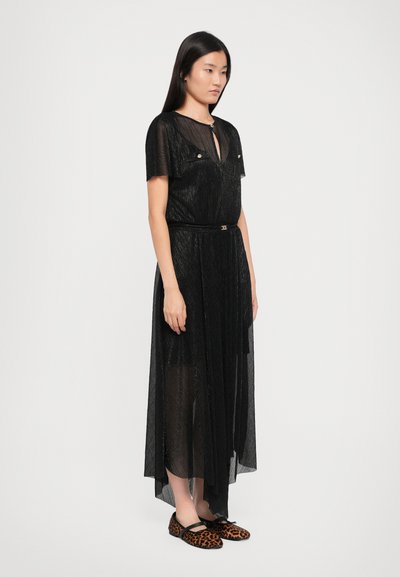 Zwarte sheer maxi jurk met korte mouwen, voorzien van een keyhole halslijn en twee borstzakken. Gecombineerd met platgekleurde schoenen met luipaardprint.