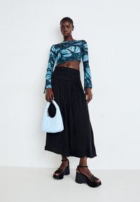 Long black skirt, blue butterfly print crop top, light blue handbag, black platform heels with straps. Smooth fabric textures and flowing design.