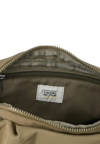 Intérieur d'un sac zippé beige avec un tissu lisse et une doublure grise. Présente une étiquette avec le logo "camel active" et des détails de couture fins.