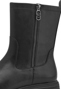 Botte en cuir noire mi-mollet avec fermeture éclair latérale en métal et languette décorative ornée d'un logo circulaire.