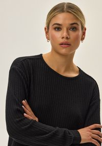 Czarny sweter prążkowany z długimi rękawami i okrągłym dekoltem, wykonany z miękkiej tkaniny o fakturowanym wykończeniu.