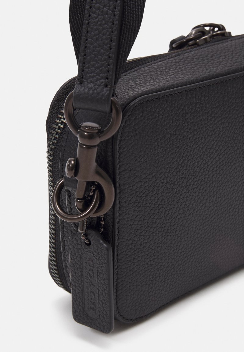 Schwarze Leder-Crossbody-Tasche mit strukturiertem Obermaterial, Reißverschluss und einem metallischen Hardwareakzent mit einem Anhänger.