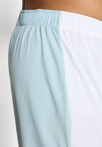 Lettvektsshorts med fargeblokkmønster i pastellblå og hvit, med elastisk midje og glatt tekstur.