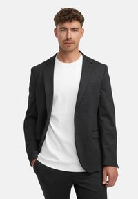 Mörkgrå kavaj med skräddarsydd passform, med slagkragar och en enkel bröstficka, bärs över en enkel vit t-shirt.