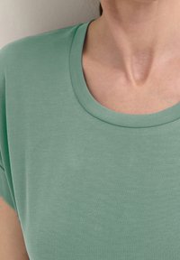 Světlounce zelené tričko s kulatým výstřihem a krátkými rukávy, vyrobené z hladké tkaniny, s jemnou strukturou a volným střihem.