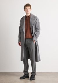 Grå hør-krave frakk med Store klapper, brun polo shirt, grå bukser og sorte sko. Glat overflade, struktureret pasform.