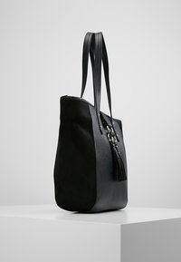 Czarna torba na ramię o g�ładkiej fakturze, z dwiema długimi uchwytami, metalowymi akcentami i dekoracyjnym frędzlem. Lekko zaokrąglony kształt.