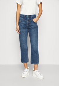 Jeans i mörkblå denim med hög midja, korta ben och klassisk femficksdesign. Matchade med vita sneakers.