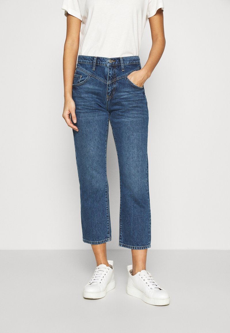 Jeans i mörkblå denim med hög midja, korta ben och klassisk femficksdesign. Matchade med vita sneakers.