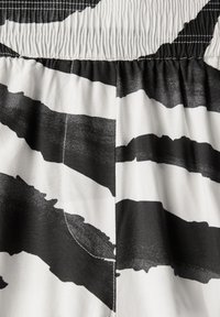 Tissu noir et blanc présentant des motifs audacieux de coups de pinceau. La taille est élastiquée avec une texture froncée.