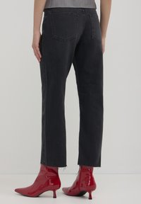 Jeans neri in denim con gamba dritta, orlo sfrangiato e tasche posteriori, abbinati a stivaletti alla caviglia a punta lucida rossi.