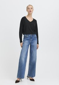 Schwarzes langärmliges V-Ausschnitt-Oberteil, kombiniert mit hellblauen weiten Jeans und braunen Spitzenschuhen. Glattes Material und entspannte Passform.