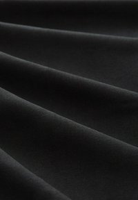 Tissu noir à texture lisse et douce présenté en gros plan avec des plis et des ombres délicats.