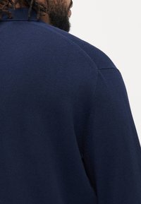 Granatowy sweter dzianinowy z okrągłym dekoltem i prążkowanymi detalami na kołnierzu oraz ramionach, charakteryzujący się gładką teksturą.