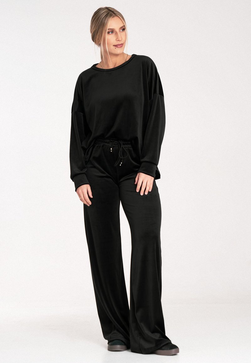 Czarny zestaw odzieży lounge z gładkiego materiału; oversize'owa koszula z długim rękawem oraz szerokie spodnie z elastycznym pasem i detalami ze sznurkiem.