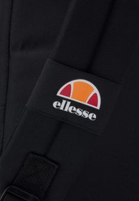Sort stofrem med et hvidt og farverigt ellesse-logo, med et orange og rødt halvcirkeldesign og en glat tekstur.