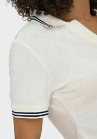 Weißes Poloshirt mit strukturierter Oberfläche, ausgestattet mit einem blau-weißen gestreiften Kragen und kurzen Ärmeln.