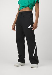 Melnas sporta bikses ar elastīgu jostu, sānu rāvējslēdzēja kabatām un baltu adidas logotipu un akcentiem. Izgatavotas no mīksta, elastīga auduma.